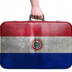 Tourist hand holding vintage leather travel bag with flag of Paraguay